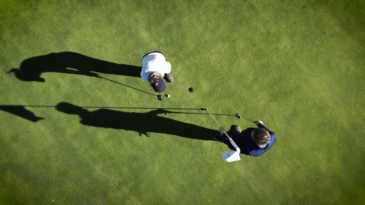Coach watching a player’s putting stroke closely beside an indoor green